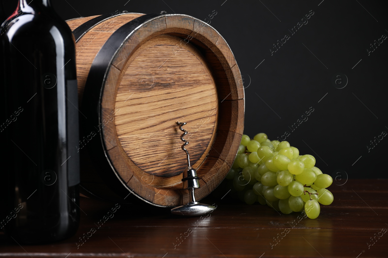 Photo of Corkscrew with metal handle, grapes, bottle of wine and barrel on wooden table