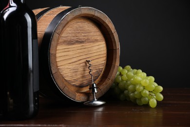 Photo of Corkscrew with metal handle, grapes, bottle of wine and barrel on wooden table