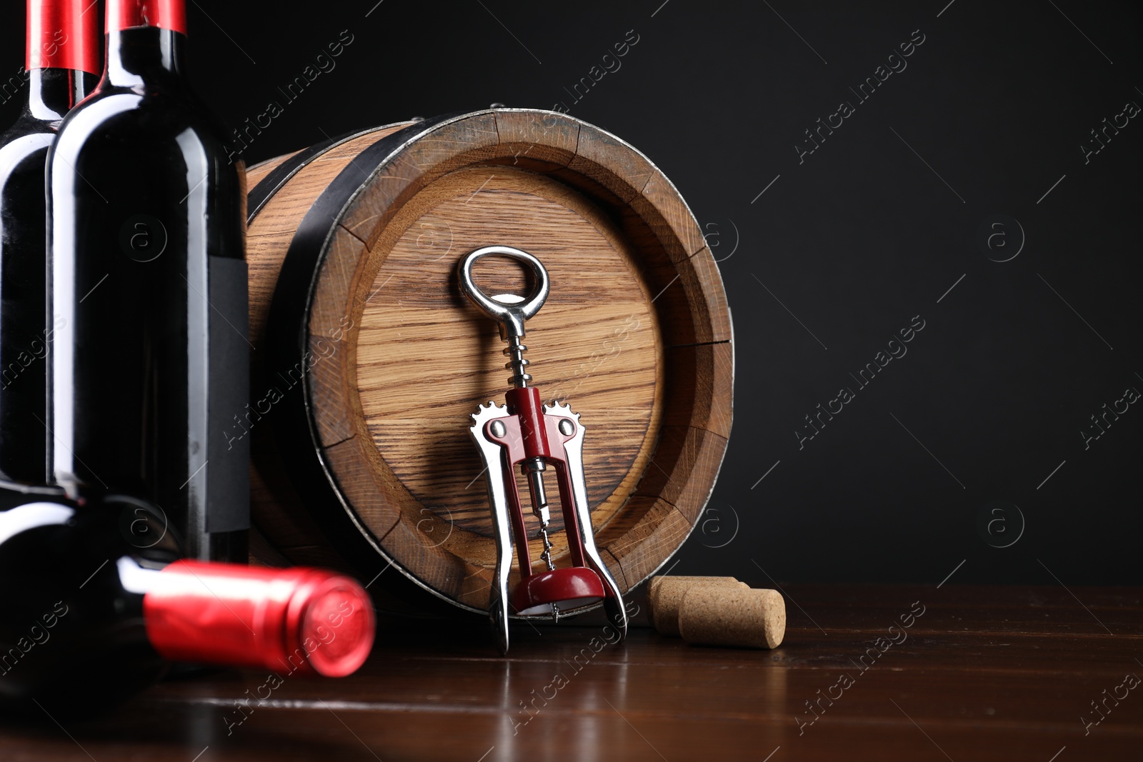 Photo of Wing corkscrew, corks, bottles of wine and barrel on wooden table. Space for text