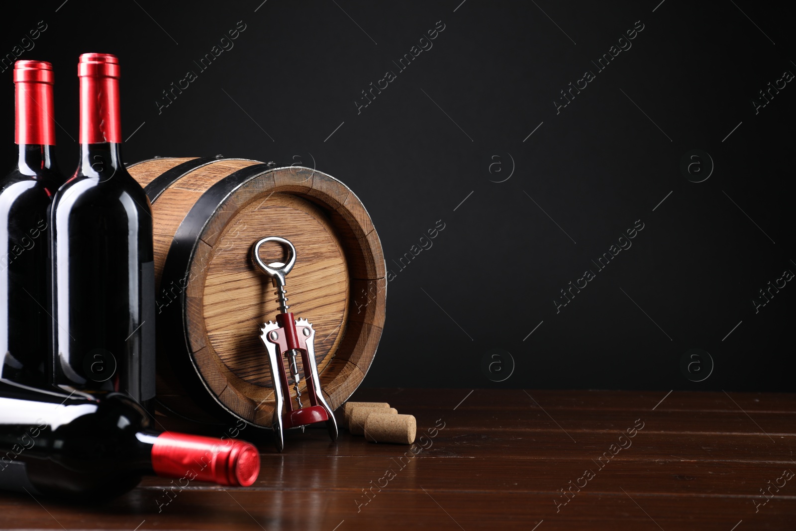 Photo of Wing corkscrew, corks, bottles of wine and barrel on wooden table, space for text