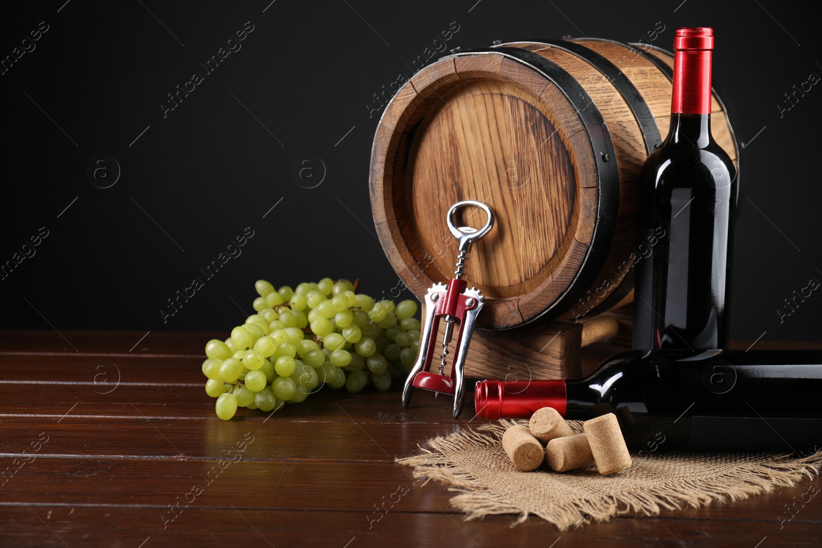 Photo of Wing corkscrew, corks, bottles of wine, grapes and barrel on wooden table