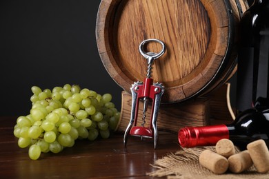 Photo of Wing corkscrew, corks, bottles of wine, grapes and barrel on wooden table