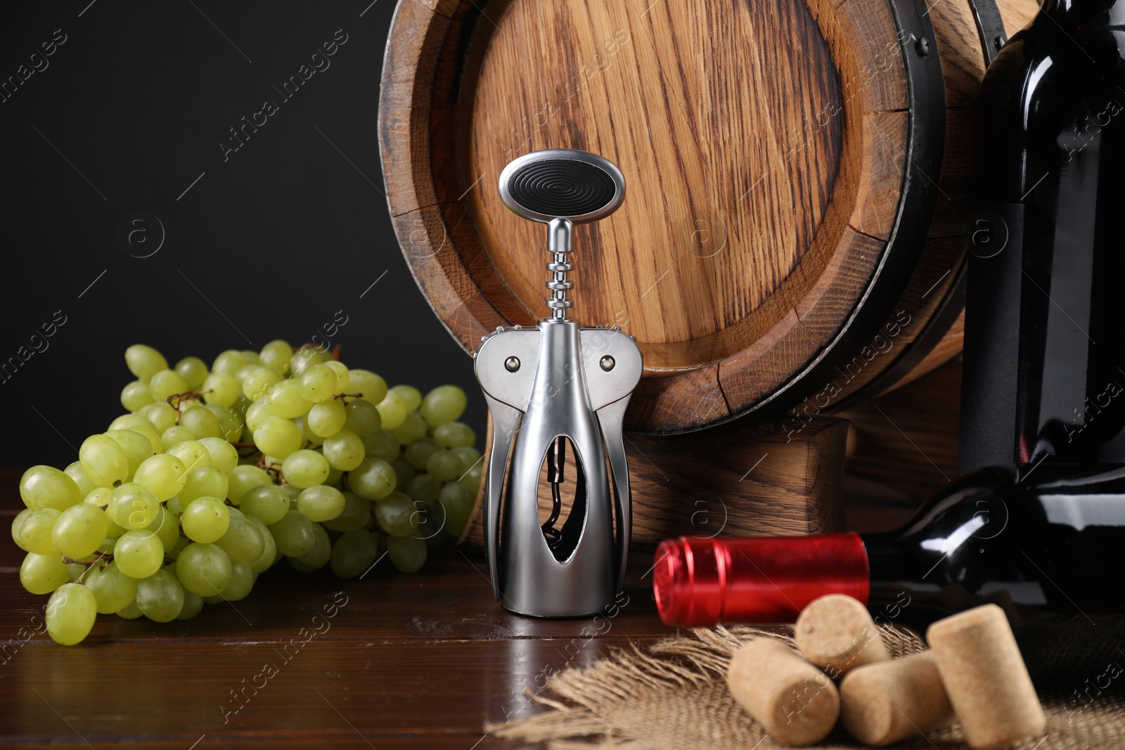 Photo of Wing corkscrew, corks, bottles of wine, grapes and barrel on wooden table