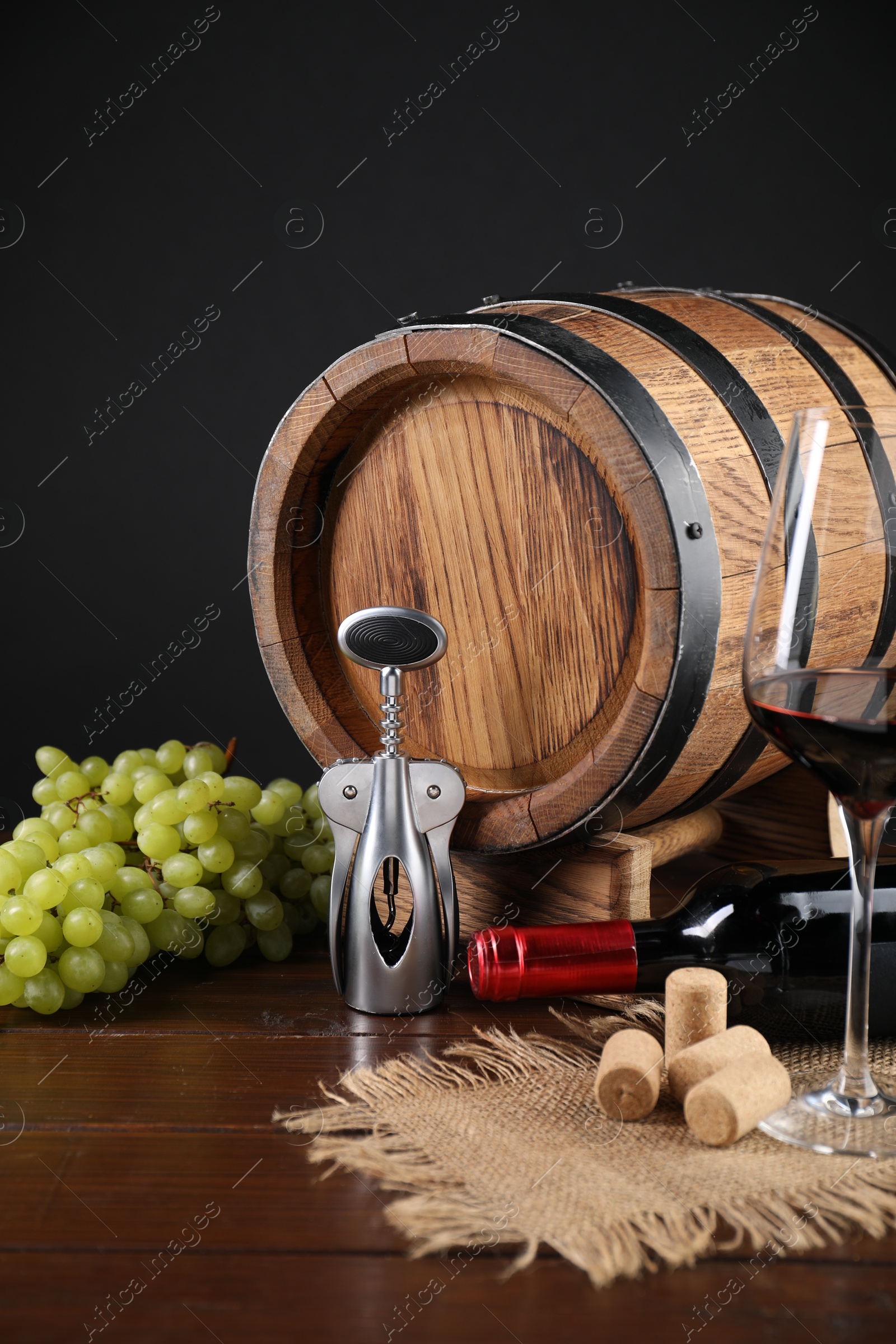 Photo of Wing corkscrew, corks, bottle of wine, glass, grapes and barrel on wooden table