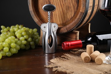 Photo of Wing corkscrew, corks, bottle of wine, glass, grapes and barrel on wooden table