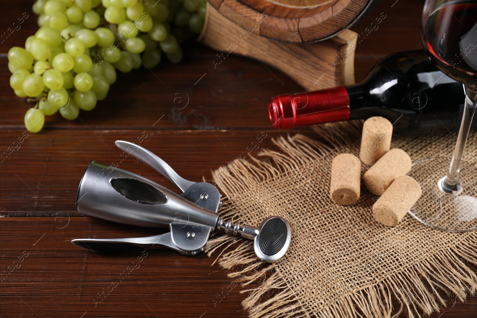 Photo of Wing corkscrew, corks, bottle of wine, glass and grapes on wooden table