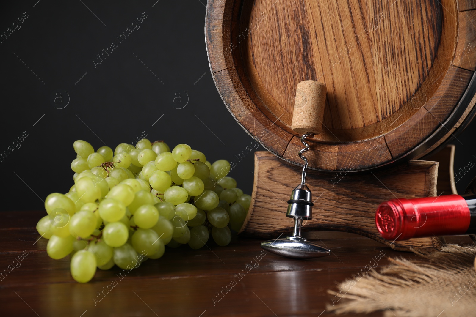 Photo of Corkscrew with metal handle, cork, grapes, barrel and bottle on wooden table