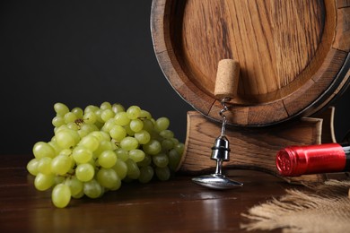 Photo of Corkscrew with metal handle, cork, grapes, barrel and bottle on wooden table