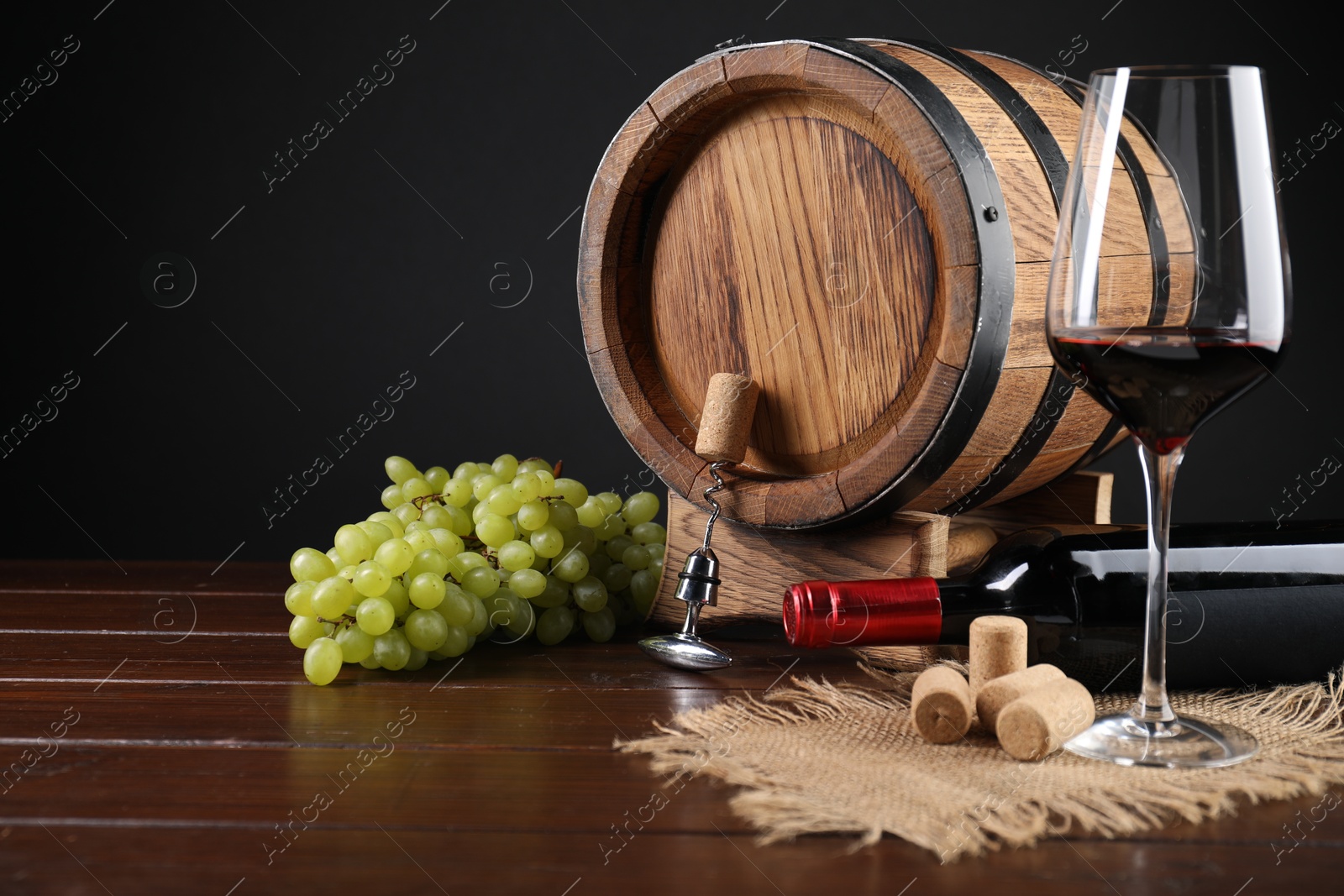 Photo of Corkscrew with metal handle, corks, bottle of wine, glass, grapes and barrel on wooden table