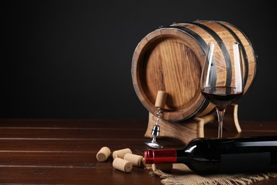 Photo of Corkscrew with metal handle, corks, bottle of wine, glass and barrel on wooden table, space for text