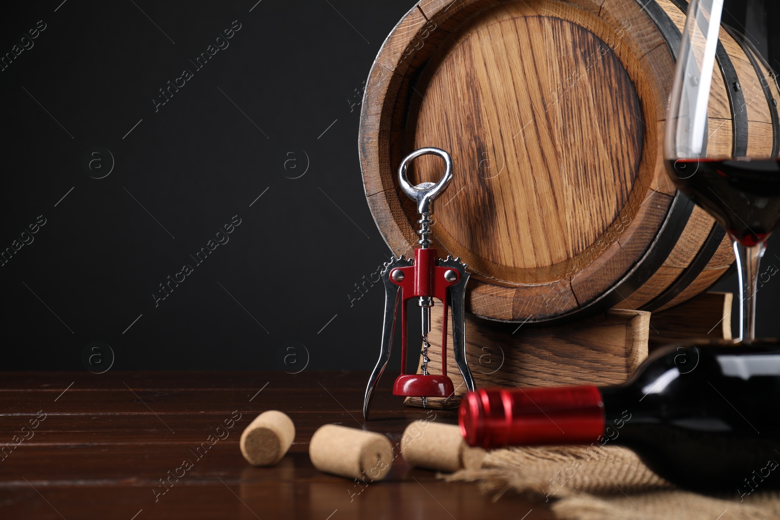 Photo of Wing corkscrew, corks, bottle of wine, glass and barrel on wooden table, space for text