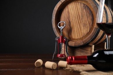 Photo of Wing corkscrew, corks, bottle of wine, glass and barrel on wooden table, space for text