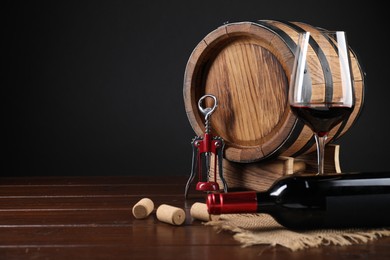 Photo of Wing corkscrew, corks, bottle of wine, glass and barrel on wooden table, space for text