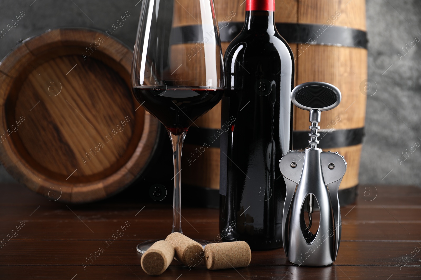 Photo of Wing corkscrew, corks, bottle of wine, glass and barrels on wooden table