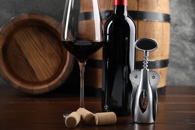 Photo of Wing corkscrew, corks, bottle of wine, glass and barrels on wooden table