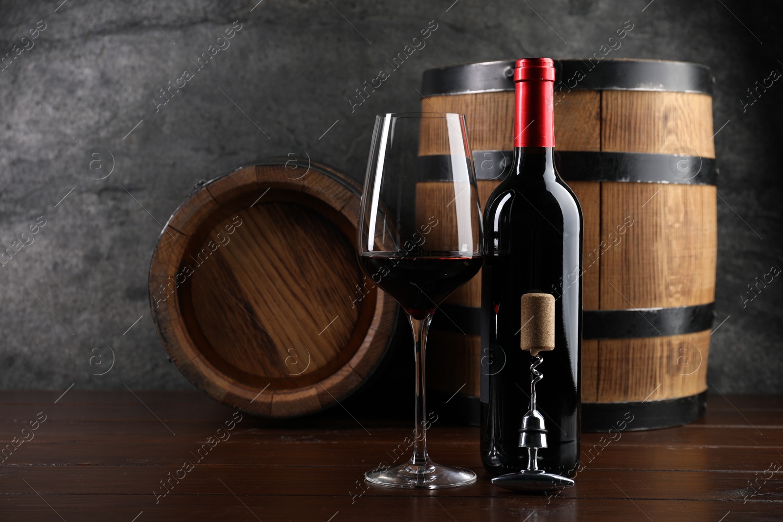 Photo of Corkscrew with metal handle, cork, bottle of wine, glass and barrels on wooden table