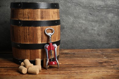 Photo of Wing corkscrew, corks and wooden barrel on table, space for text