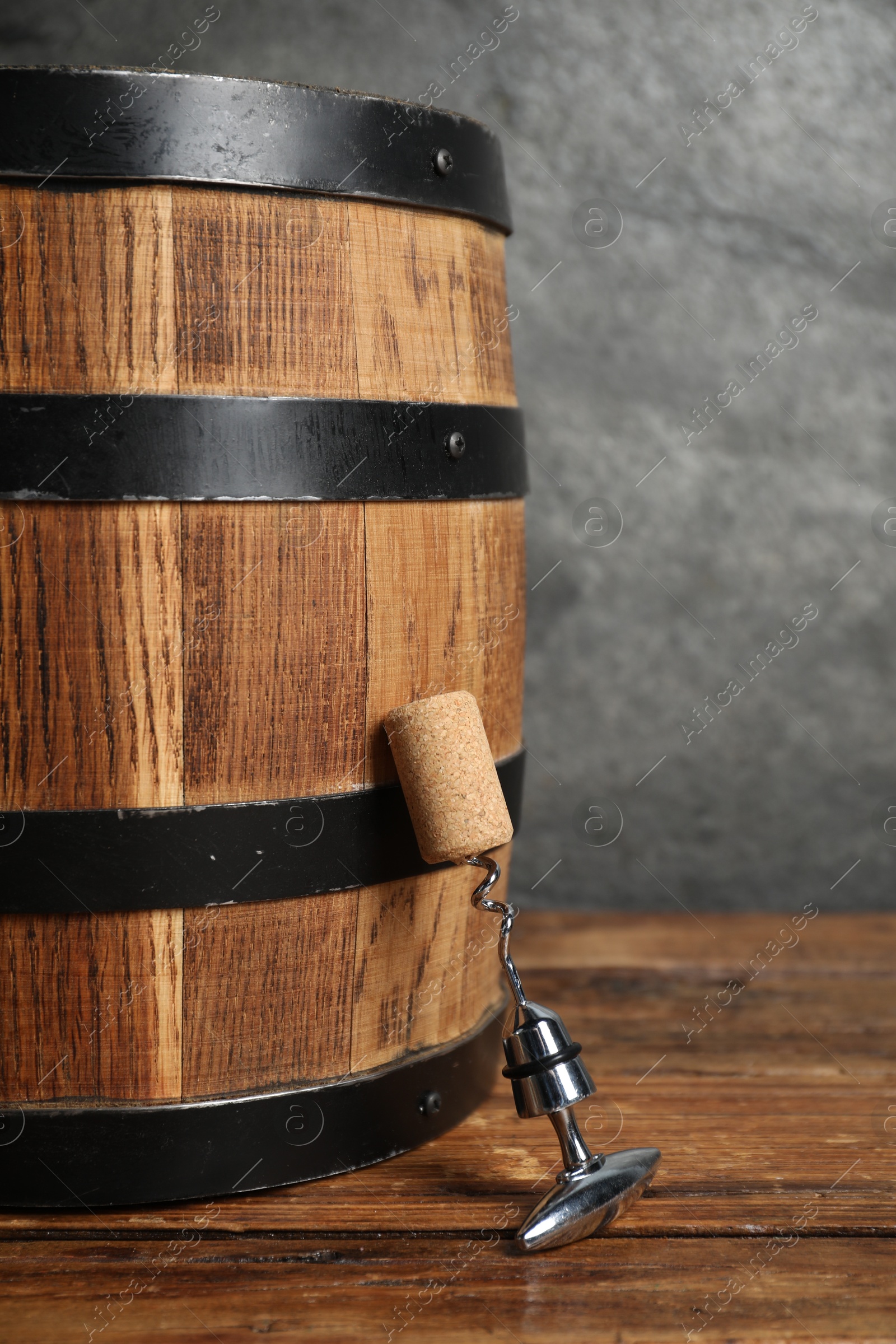 Photo of Corkscrew with metal handle, cork and wooden barrel on table