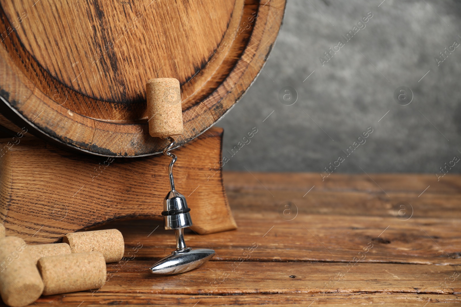 Photo of Corkscrew with metal handle, corks and wooden barrel on table, space for text