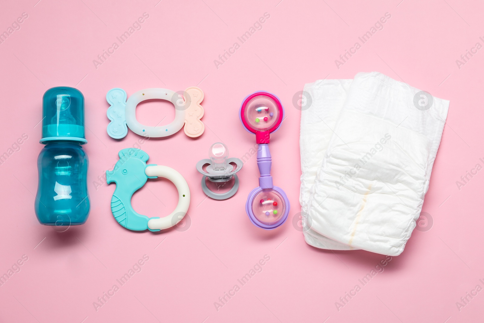 Photo of Colorful rattles, diapers, bottle and pacifier on pale pink background, flat lay. Baby accessories