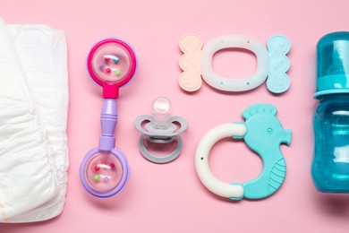 Photo of Colorful rattles, diapers, bottle and pacifier on pale pink background, flat lay. Baby accessories