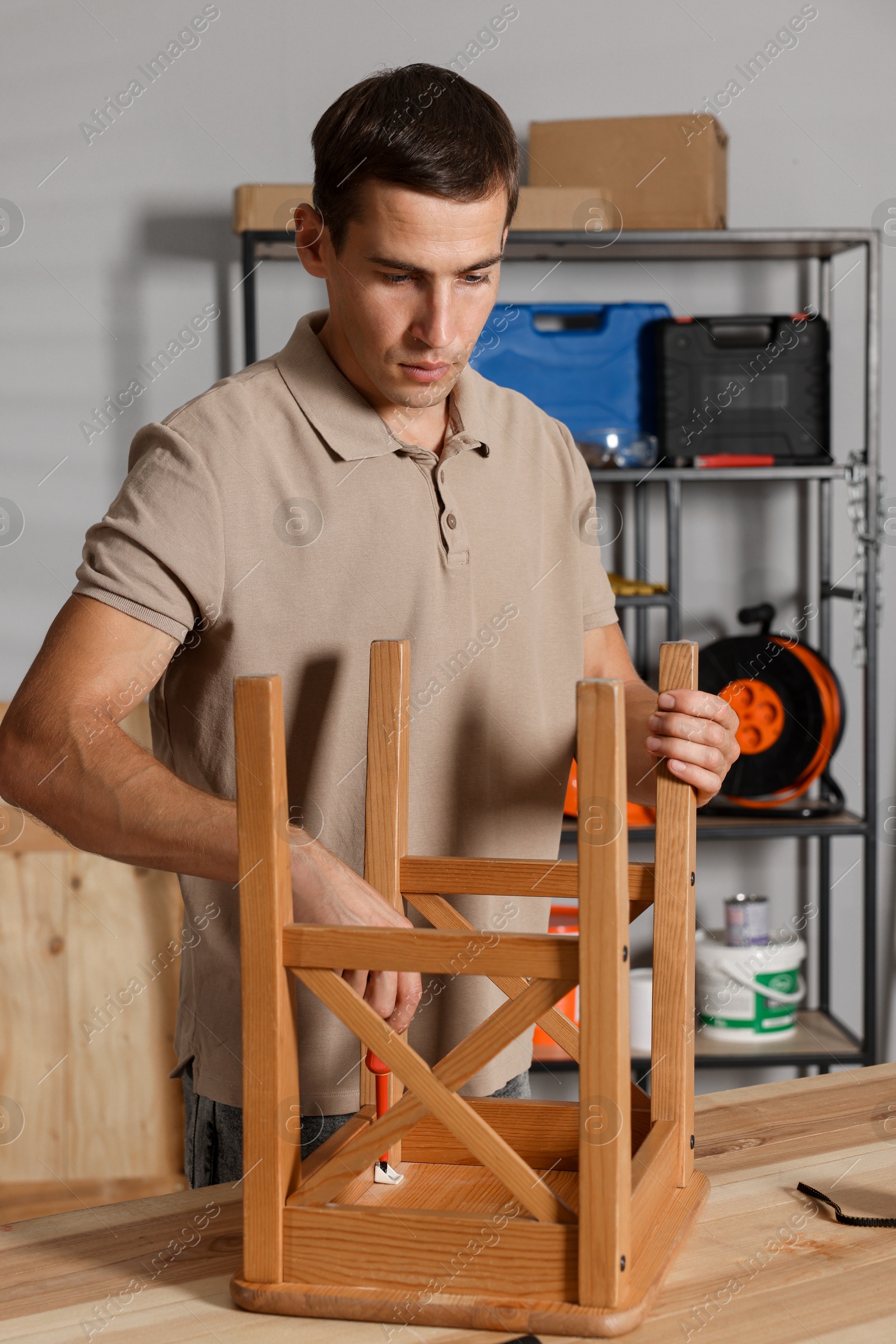 Photo of Man repairing wooden stool with screwdriver indoors