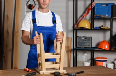 Photo of Man repairing wooden stool at table indoors, closeup