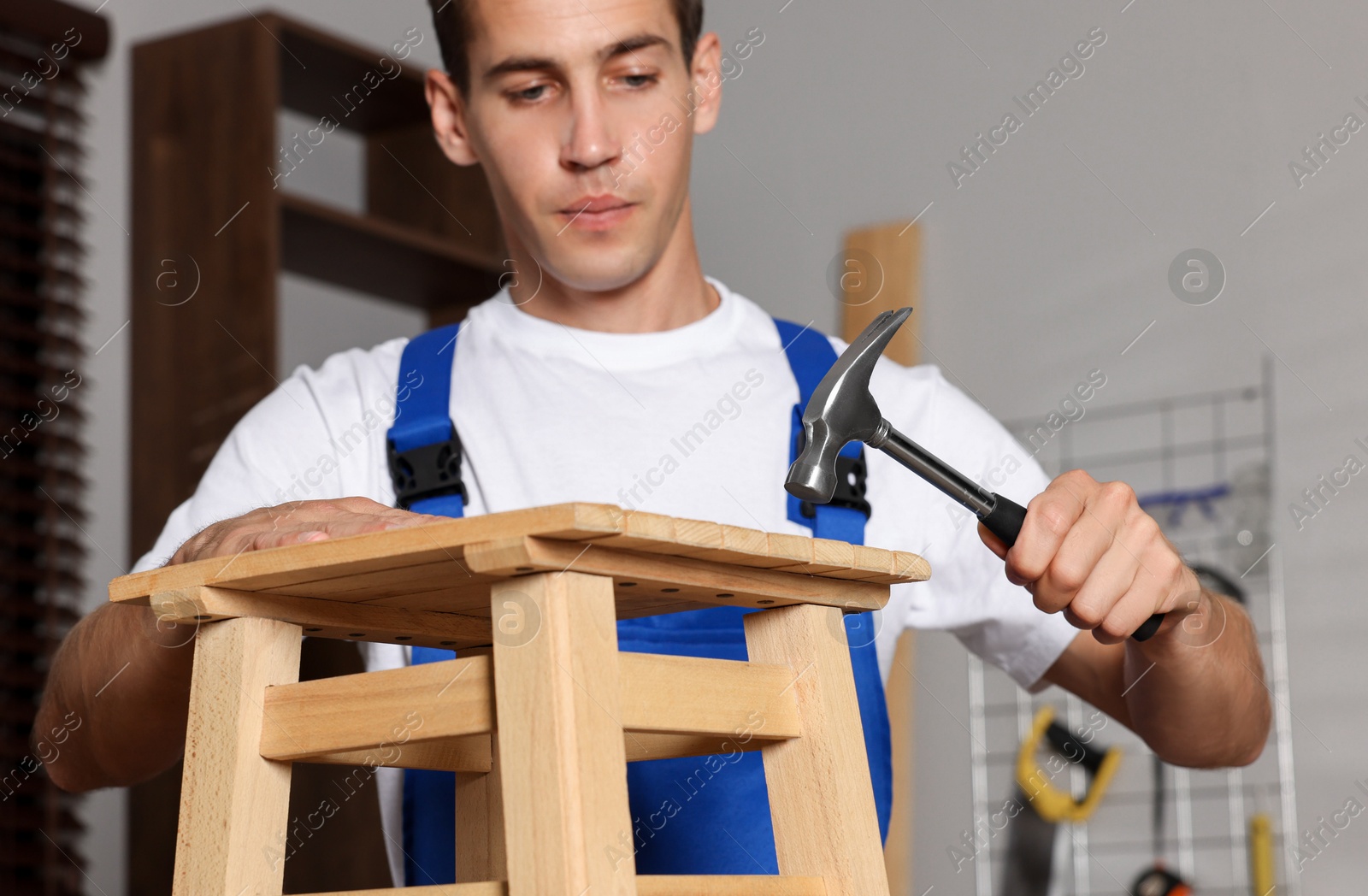 Photo of Man repairing wooden stool with hammer indoors