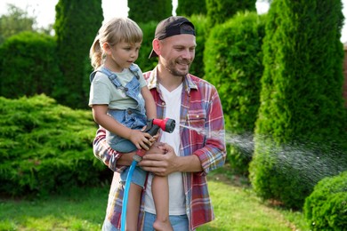 Father and his daughter watering lawn with hose in backyard