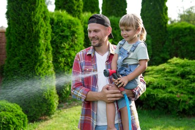 Photo of Father and his daughter watering lawn with hose in backyard