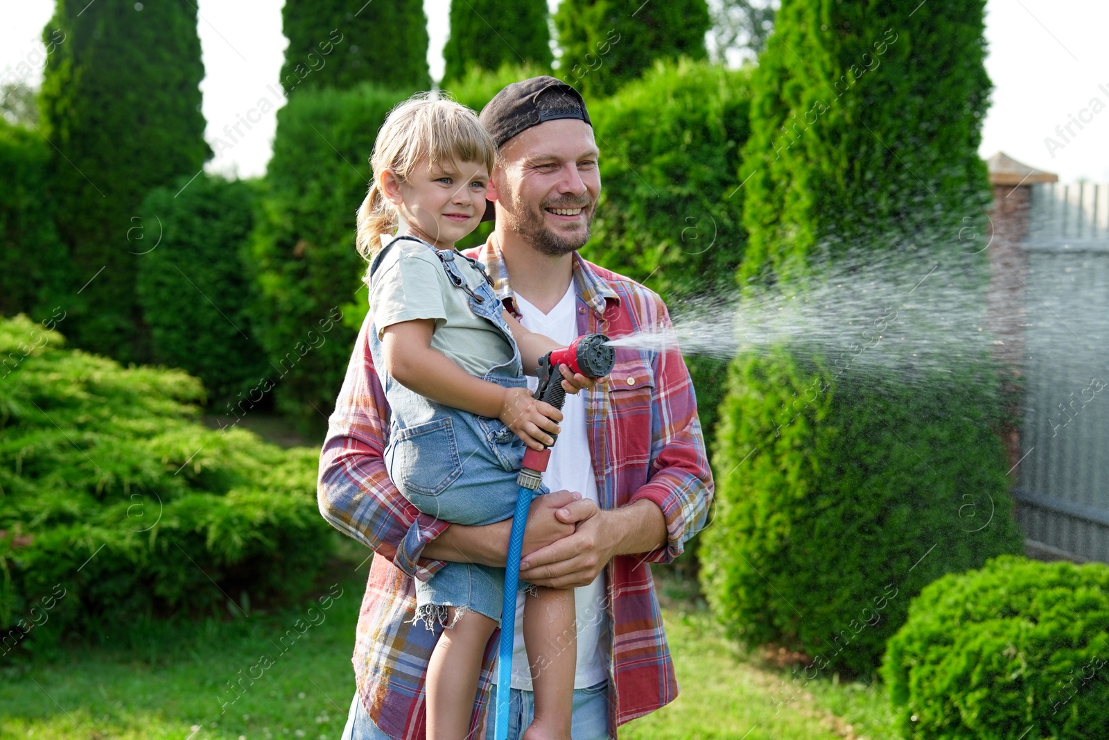 Photo of Father and his daughter watering lawn with hose in backyard