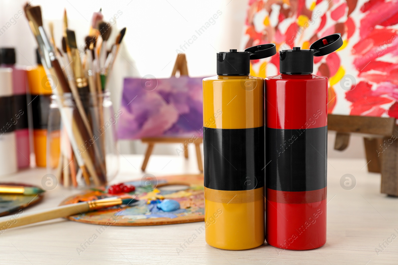 Photo of Acrylic paints of different colors, small easels, palette and brushes on wooden table indoors