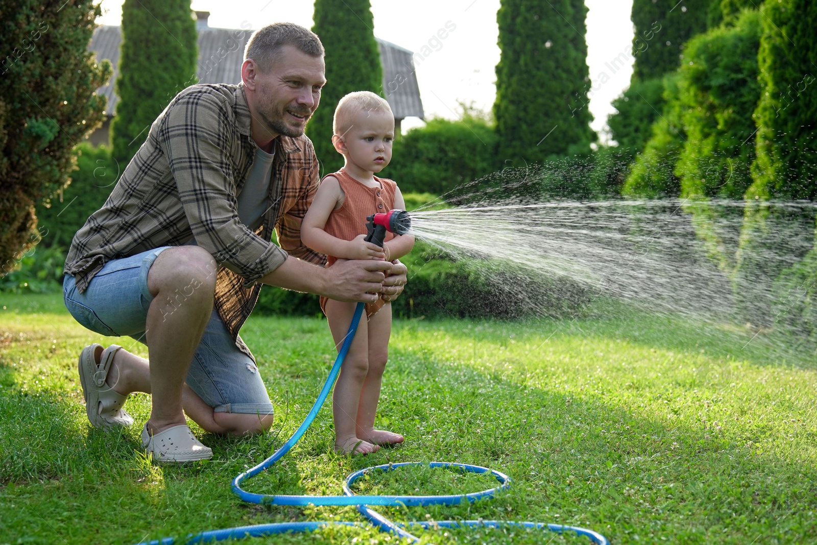 Photo of Father and his son watering lawn with hose in backyard