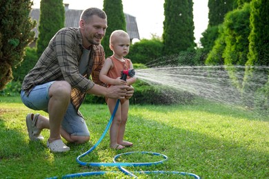 Father and his son watering lawn with hose in backyard