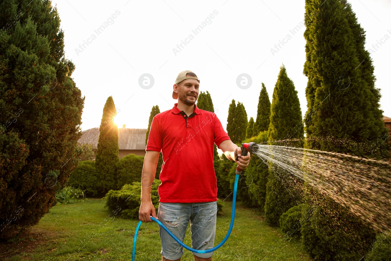 Photo of Man watering lawn with hose in backyard