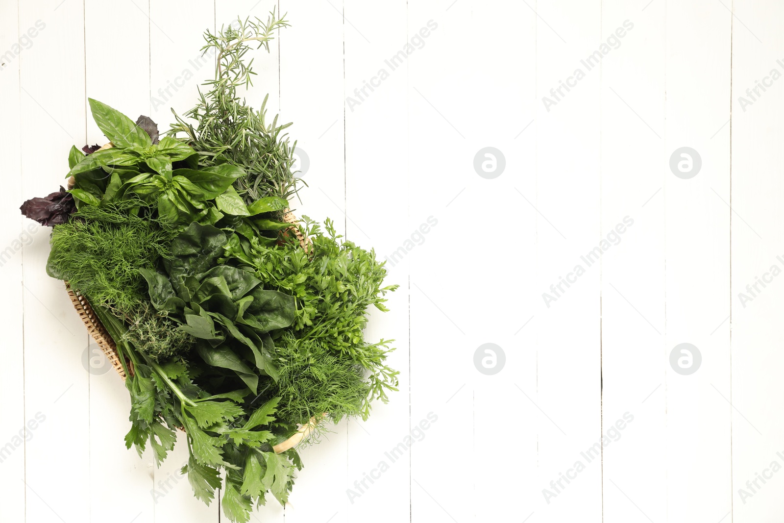 Photo of Different fresh herbs in basket on white wooden table, top view. Space for text