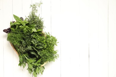 Photo of Different fresh herbs in basket on white wooden table, top view. Space for text