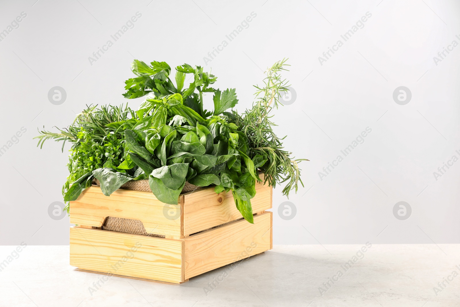 Photo of Different fresh herbs in wooden basket on white table. Space for text