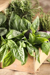 Different fresh herbs in basket on wooden table, closeup