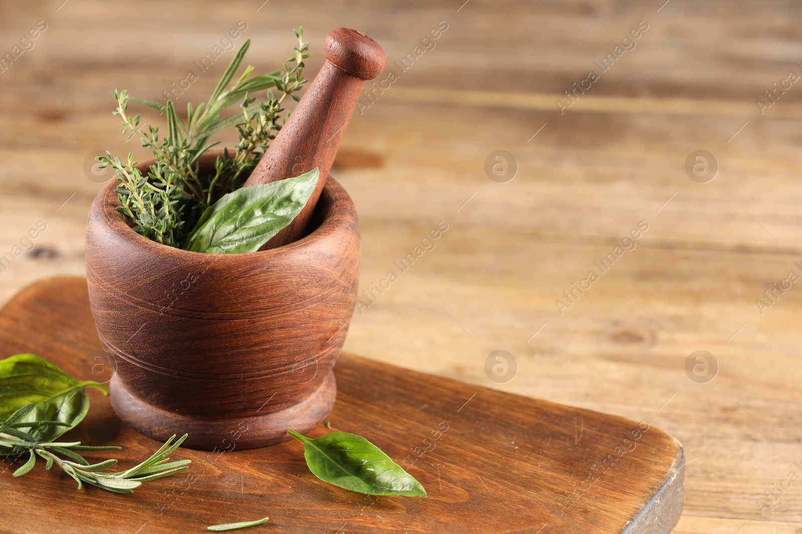 Photo of Different fresh herbs in mortar with pestle on wooden table, space for text