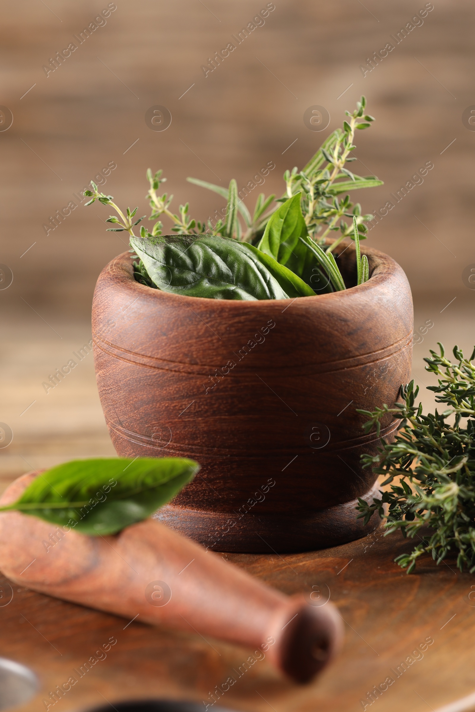 Photo of Different fresh herbs in mortar with pestle on wooden table, closeup