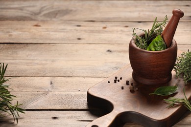 Photo of Different fresh herbs in mortar with pestle on wooden table, space for text