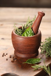 Photo of Different fresh herbs in mortar with pestle on wooden table