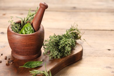 Photo of Different fresh herbs in mortar with pestle on wooden table, space for text