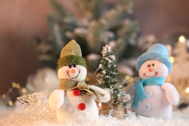 Photo of Funny snowman figures and decorative Christmas tree on artificial snow against blurred background