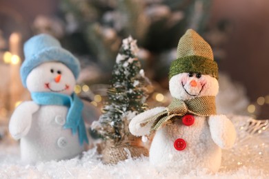 Photo of Funny snowman figures and decorative Christmas tree on artificial snow against blurred background