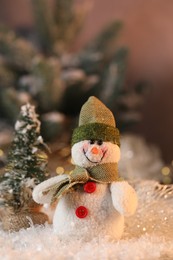 Photo of Funny snowman figure and decorative Christmas tree on artificial snow against blurred background