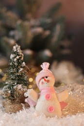 Photo of Funny snowman figure and decorative Christmas tree on artificial snow against blurred background