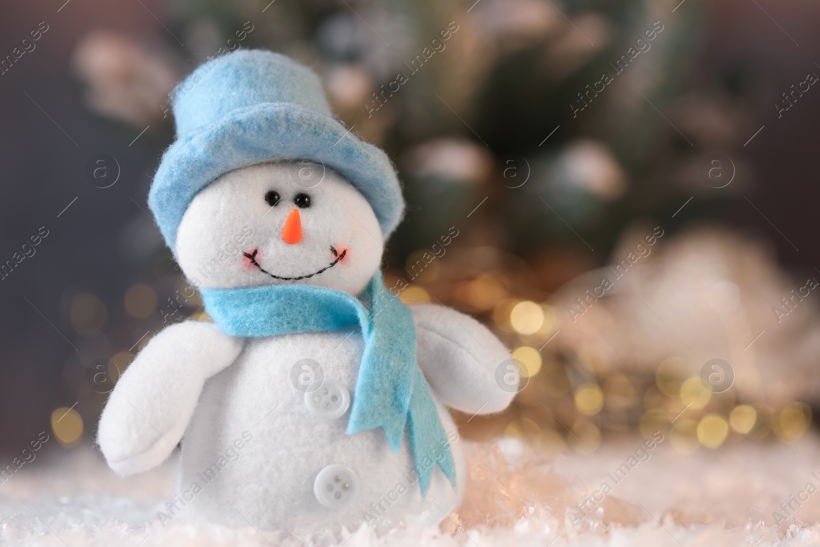 Photo of Funny snowman figure on artificial snow against blurred lights, closeup