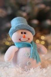 Photo of Funny snowman figure on artificial snow against blurred lights, closeup